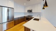 Located at 703 Whitney Ave in New Haven, CT, this single-floor 1-bedroom, 1-bathroom residence offers a thoughtfully designed open-concept layout with clean modern finishes throughout. Rich hardwood flooring extends across the living and dining areas, complemented by recessed lighting and crisp white walls that create a bright, airy atmosphere.

The kitchen is a standout feature, showcasing dual-tone cabinetry with high-gloss white upper cabinets and warm wood-finish lower cabinets, paired with sleek white quartz countertops and a glass tile backsplash. Stainless steel appliances — including a gas range, microwave, and refrigerator — complete the space, while a large island with a undermount sink and stylish pendant lighting adds both function and character.

The bedroom offers a calm, light-filled retreat with soft blue-gray walls, hardwood floors, and a window framing views of the surrounding New Haven neighborhood. An in-unit stacked washer and dryer is conveniently tucked behind a dedicated closet door near the main living area.

The bathroom is elegantly finished with large-format marble-look tile, a frameless glass walk-in shower, modern wall sconces, and a floating vanity with an undermount sink and wide mirror, delivering a spa-like experience.
