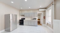 Located at 81 Academy St in Poughkeepsie, NY, this single-floor residence offers three bedrooms, one bathroom, a kitchen, and two hallways within a compact yet functional layout. The kitchen is a standout feature, equipped with gray shaker-style cabinetry, white countertops, a stainless steel refrigerator, and a black range, all set atop large-format white tile flooring with recessed ceiling lighting that brightens the space. A wall-mounted mini-split unit provides additional climate control, complementing the classic cast-iron radiators found throughout the home. The bedrooms feature warm-toned hardwood flooring and neutral wall colors, with the primary bedroom offering a generous footprint and natural light from a window with views to the outdoors. The hallways connect the rooms efficiently and also showcase the home's hardwood floors and classic six-panel white doors. The bathroom includes a tub-shower combination with elegant marble-style tile surround walls. A staircase with a wooden banister is visible in one hallway area, along with a built-in closet for added storage. Overall, the home blends classic architectural details with updated finishes, creating a practical and inviting living environment.