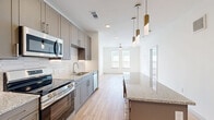 This thoughtfully designed 1-bedroom, 1-bathroom residence offers a clean, modern aesthetic throughout its single floor. The open-concept kitchen and living area serves as the heart of the home, featuring gray shaker-style cabinetry, granite countertops, a hexagonal tile backsplash, and a full suite of stainless steel appliances. A central kitchen island with pendant lighting in brushed gold adds both style and functionality, while light hardwood-style flooring runs throughout the common areas, creating a warm, cohesive feel. The living area extends naturally from the kitchen, brightened by multiple windows and a ceiling fan overhead.

The bedroom is a calm, carpeted retreat with soft neutral tones, multiple windows that invite natural light, and a ceiling fan for comfort. A dedicated closet provides convenient storage.

The bathroom is generously proportioned, showcasing dual granite-topped vanities with gray cabinetry, a large mirror with overhead lighting, light hardwood flooring, and a marble-surround tub and shower enclosure. An in-unit laundry area adds everyday practicality. Clean white walls, modern hardware, and consistent finishes throughout give this residence a polished, move-in-ready appeal.