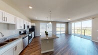 This well-appointed single-floor residence showcases a thoughtfully designed open-concept layout that seamlessly connects the kitchen and living areas. The kitchen is a standout feature, equipped with stainless steel appliances including a refrigerator, range, and microwave, all complemented by crisp white shaker cabinetry, granite countertops, and a large center island with pendant lighting overhead. Rich dark hardwood-style flooring flows throughout the main living spaces, adding warmth and continuity to the interior.

The spacious living area is bathed in natural light, courtesy of large sliding glass doors that open onto a private balcony, offering sweeping outdoor views of the surrounding landscape. Multiple bedrooms are carpeted for comfort, each featuring sliding glass doors or large windows that invite natural light and outdoor scenery. Bedroom closets provide ample storage with built-in shelving and hanging rods.

The bathrooms are finished with granite-topped vanities, white cabinetry, and hardwood-style flooring, with one bathroom featuring a full tub and shower combination. The neutral warm-toned walls throughout the residence create a clean, cohesive ambiance that is both inviting and versatile, making this a highly functional and visually appealing living space.