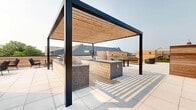 Located at 1 Cemetery St in Norwalk, CT, this thoughtfully designed rooftop terrace offers a seamless blend of comfort and modern outdoor living. The space is divided into two distinct yet complementary zones, each crafted to maximize relaxation and entertainment.

The turf zone features a vibrant stretch of lush artificial grass bordered by natural cedar wood-clad walls that provide both privacy and warmth. Several teak-framed chaise lounges with charcoal cushions are arranged to take full advantage of the open sky above, creating an ideal sunbathing retreat. A utility shed with a roll-up door sits neatly at the far end, complementing the clean aesthetic.

Transitioning seamlessly to the second zone, large-format porcelain tiles underfoot set an elegant tone for the lounge and dining area. Stylish rope-woven outdoor seating anchors a casual conversation area, while a pergola-covered bar extends across the background, offering a defined space for dining and entertaining. The horizontal cedar accent walls unify both areas with rich, natural texture, and wall-mounted lighting adds ambiance for evening use.

Together, the two zones create a cohesive and versatile rooftop destination with open views of the surrounding Norwalk landscape and clear, open skies above.