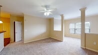 Located at 101 Carden Place Dr in Mebane, NC, this single-floor residence offers a well-designed layout with consistent warm neutral tones and plush carpet flooring throughout. The main living area is a standout, featuring elegant crown molding, a decorative column detail that defines separate zones within the open floor plan, and a ceiling fan with light fixture. Natural light filters in through windows with blinds, creating a bright and welcoming atmosphere. An additional carpeted room, also equipped with a ceiling fan and window, provides flexible living or sleeping space. The bedroom includes access to a walk-in closet with built-in shelving and a private en suite bathroom. The bathrooms are finished with warm wood-toned cabinetry, white countertops, a single-sink vanity, and louvered medicine cabinet doors. The kitchen is functional and well-equipped, featuring light maple cabinetry, dark granite-style countertops, and stainless steel appliances including a refrigerator, electric range, and over-the-range microwave. Wood-look flooring in the kitchen and bath areas complements the carpeted living spaces. The overall layout, viewed from above, reveals a thoughtfully organized floor plan that balances open communal areas with private living quarters.