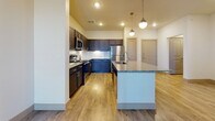 This single-floor residence offers a well-designed layout with contemporary finishes throughout. The kitchen serves as a central highlight, showcasing dark espresso cabinetry paired with granite countertops and a matching large island with an undermount sink. Stainless steel appliances, including a gas range, microwave, and refrigerator, complement the space, while globe pendant lights suspended above the island add a modern, stylish touch. A white tile backsplash and under-cabinet lighting further enhance the kitchen's polished aesthetic. Wood-look plank flooring flows throughout the main living areas, contributing warmth and visual continuity.

The bedroom features soft carpeting and benefits from natural light through dual windows fitted with horizontal blinds, offering a quiet and comfortable retreat. The bathroom is thoughtfully appointed with a granite-topped vanity, dark cabinetry with brushed nickel hardware, a large mirror with overhead lighting, and a full tub-shower combination. Light wood-look flooring extends into the bathroom, maintaining design consistency. Together, the spaces reflect a cohesive modern aesthetic with quality materials and functional layouts throughout.