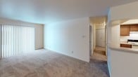 This two-bedroom, one-and-a-half-bathroom residence is thoughtfully laid out across a single floor, offering a comfortable and practical living environment. The spacious living area features neutral-toned carpet and a large vertical-blind window that allows natural light to fill the room, creating a bright and open atmosphere. A dedicated entryway with a paneled front door provides a welcoming point of entry. The kitchen is well-equipped with rich, warm-toned wood cabinetry, light stone-finish countertops, a coil-top range, and a stainless steel sink — offering ample storage and functional workspace. Both bedrooms are generously sized, finished with plush carpet and windows fitted with blinds. The primary bedroom includes access to a full bathroom and features a louvered closet, while a secondary bathroom with a vanity and large mirror serves additional needs. The full bathroom includes a tiled shower-tub combination with a curved curtain rod. A hallway connects the bedrooms and bathrooms, maximizing the efficient flow of the floor plan. Throughout, the clean white walls and neutral palette create a versatile backdrop well-suited to a variety of interior styles.