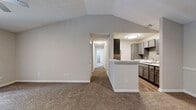 This single-story, 3-bedroom, 2-bathroom home offers a thoughtfully designed layout with a comfortable and functional flow throughout. The living room serves as the heart of the home, featuring dramatic vaulted ceilings that lend a sense of openness and volume, soft carpet flooring, and a tile-surround fireplace that provides a welcoming focal point. Natural light enters through the front entry area, which connects seamlessly to the rest of the floor plan via a central hallway.

The galley-style kitchen is well-equipped with gray shaker cabinetry, marble-look countertops, a tile backsplash, and wood-look flooring. A kitchen peninsula provides a transition into the open living area, enhancing the connected feel of the shared space.

The three bedrooms are carpeted and receive natural light through sizable windows with views of surrounding greenery. Each room offers a calm, neutral palette suitable for a variety of uses. Three closets provide ample storage throughout.

Two full bathrooms each include a tiled tub/shower combination, modern gray vanities, and wood-look flooring, maintaining a consistent, clean aesthetic. A dedicated laundry room accommodates a full-size side-by-side washer and dryer with overhead wire shelving for additional storage. Two hallways connect the private areas of the home efficiently to the main living spaces.