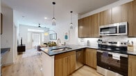 This well-appointed 1-bedroom, 1-bathroom unit offers a thoughtfully designed open-concept layout across a single floor, maximizing every square foot with modern finishes and a clean, contemporary aesthetic. Light wood flooring runs throughout, tying each room together cohesively.

The kitchen is a standout feature, showcasing warm wood cabinetry, dark quartz countertops, a marble-style tile backsplash, and a full suite of stainless steel appliances including a range, over-the-range microwave, dishwasher, and refrigerator. A peninsula with a dark countertop and bar seating—illuminated by stylish pendant lights—creates an inviting space for dining or entertaining, and flows directly into the open living room.

The living room benefits from abundant natural light provided by large windows with plantation shutters and a glass patio door, topped with a transom window. A ceiling fan overhead and warm, layered lighting complete the comfortable atmosphere.

The bedroom is a well-sized retreat featuring a ceiling fan, large windows with blinds and drape panels, and warm wood flooring. An adjacent walk-in closet offers ample shelving and hanging storage.

The bathroom features a clean, modern design with a dark vanity, white quartz countertop, large mirror, and a tub-shower combo accented by geometric white tile. Every room reflects a consistent, polished design sensibility throughout.