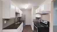 This renovated Phase II unit offers two bedrooms and one bathroom thoughtfully arranged across a single floor. The galley-style kitchen is a standout feature, showcasing dark granite countertops, crisp white shaker cabinetry with brushed nickel hardware, and a classic subway tile backsplash in a warm grey tone. Stainless steel appliances — including a refrigerator, dishwasher, and electric range — provide a sleek, functional cooking environment. Dark wood-style flooring runs the length of the kitchen, adding warmth and contrast against the light grey walls. A double stainless steel sink with a modern faucet completes the kitchen's clean aesthetic. The textured ceiling adds a traditional touch throughout the space. The overall design palette of the unit is neutral and contemporary, combining updated fixtures and finishes that reflect the Phase II renovation upgrades. The single-floor layout ensures easy navigation between living, sleeping, and functional areas, making this unit a practical and attractive option for those seeking a move-in-ready, modernized home.