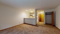 Located at 1218 McKenna Blvd in Madison, Wisconsin, this single-floor unit offers a straightforward, functional layout designed for comfortable everyday living. The main living area is generously proportioned, featuring neutral wall-to-wall carpeting, clean white walls, and recessed lighting that keeps the space feeling bright and open. A wall-mounted HVAC unit provides climate control, and a sliding glass door leads directly to a private patio overlooking a lush, tree-lined green space, bringing natural light and outdoor views into the room.

The kitchen is designed in a galley configuration, accessible via a peninsula-style pass-through counter that connects it to the living area. It is equipped with white cabinetry, a full-size refrigerator, an electric coil range with overhead ventilation, and a dishwasher. Tile flooring with a stone-like pattern runs throughout the kitchen, adding a practical and easy-to-clean surface.

The hallway leads to the bedroom, which includes a closet with wood-tone doors. The full bathroom features tile flooring consistent with the kitchen, a white vanity with built-in storage, a toilet, and a full tub-shower combination with a grab bar, offering added accessibility. Warm wood-tone doors and trim accents appear throughout, providing cohesion across the unit.