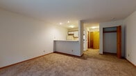 Located at 1218 McKenna Blvd in Madison, Wisconsin, this single-floor unit offers a straightforward, functional layout designed for comfortable everyday living. The main living area is generously proportioned, featuring neutral wall-to-wall carpeting, clean white walls, and recessed lighting that keeps the space feeling bright and open. A wall-mounted HVAC unit provides climate control, and a sliding glass door leads directly to a private patio overlooking a lush, tree-lined green space, bringing natural light and outdoor views into the room.

The kitchen is designed in a galley configuration, accessible via a peninsula-style pass-through counter that connects it to the living area. It is equipped with white cabinetry, a full-size refrigerator, an electric coil range with overhead ventilation, and a dishwasher. Tile flooring with a stone-like pattern runs throughout the kitchen, adding a practical and easy-to-clean surface.

The hallway leads to the bedroom, which includes a closet with wood-tone doors. The full bathroom features tile flooring consistent with the kitchen, a white vanity with built-in storage, a toilet, and a full tub-shower combination with a grab bar, offering added accessibility. Warm wood-tone doors and trim accents appear throughout, providing cohesion across the unit.