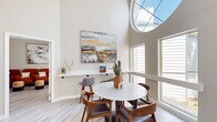 Located at 11800 Montgomery Blvd NE in Albuquerque, New Mexico, this thoughtfully designed single-floor space makes a strong architectural statement from the moment you enter. The standout feature is a dramatic oversized circular skylight that crowns the main gathering area, flooding the space with abundant natural light and drawing the eye upward to the soaring ceilings above. Light-toned hardwood-style flooring runs throughout, complementing the warm, neutral color palette of the walls and contributing to the space's airy, welcoming ambiance.

The main area is anchored by a marble-top round dining table surrounded by mid-century modern wooden chairs, positioned directly beneath the skylight. A built-in floating shelf displays curated décor, while large windows along the walls frame views of the surrounding greenery. A separate lounge area features a plush sectional sofa, a solid wood coffee table, and a pair of accent chairs, all arranged around a pool table — making this an ideal space for recreation and socializing. A cluster of bold terracotta-hued armchairs adds a vibrant pop of color to a dedicated seating nook, accented by contemporary abstract artwork. The overall design blends modern comfort with artistic flair, creating a versatile and inviting environment.