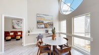 Located at 11800 Montgomery Blvd NE in Albuquerque, New Mexico, this thoughtfully designed single-floor space makes a strong architectural statement from the moment you enter. The standout feature is a dramatic oversized circular skylight that crowns the main gathering area, flooding the space with abundant natural light and drawing the eye upward to the soaring ceilings above. Light-toned hardwood-style flooring runs throughout, complementing the warm, neutral color palette of the walls and contributing to the space's airy, welcoming ambiance.

The main area is anchored by a marble-top round dining table surrounded by mid-century modern wooden chairs, positioned directly beneath the skylight. A built-in floating shelf displays curated décor, while large windows along the walls frame views of the surrounding greenery. A separate lounge area features a plush sectional sofa, a solid wood coffee table, and a pair of accent chairs, all arranged around a pool table — making this an ideal space for recreation and socializing. A cluster of bold terracotta-hued armchairs adds a vibrant pop of color to a dedicated seating nook, accented by contemporary abstract artwork. The overall design blends modern comfort with artistic flair, creating a versatile and inviting environment.