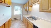 Located at 1615 N Winton Rd in Rochester, NY, this single-floor unit offers a well-organized layout with a variety of practical features throughout. The spacious living area is highlighted by rich hardwood flooring that extends across the main living spaces, complemented by large windows fitted with vertical blinds that allow generous natural light to fill the room. A wall-mounted HVAC unit and baseboard heating provide year-round climate control, while a ceiling fan adds to the comfort of an additional room near the entry door, which also includes a closet with louvered doors.

The kitchen is outfitted with light wood cabinetry offering ample storage both above and below the countertops. A stainless steel sink, under-cabinet lighting, and a window overlooking the outdoors make this a functional and pleasant workspace. Light tile flooring completes the kitchen's clean aesthetic.

The bedroom features wall-to-wall carpeting for warmth and comfort, along with a window that brings in natural light and baseboard heating along the perimeter.

The bathroom presents classic white subway tile walling around the tub surround, a mosaic tile floor in soft yellow tones, a white vanity, and a window for natural ventilation, creating a bright and tidy space.