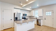 This well-designed two-story home offers 2 bedrooms, 3 bathrooms, and a thoughtful layout spread across two floors. The main level features an open-concept kitchen and living area with light hardwood-style flooring throughout. The kitchen is a standout, boasting crisp white shaker cabinetry, a white subway tile backsplash, a central island with a quartz-style countertop and bar seating, and a full suite of stainless steel appliances including a refrigerator with ice maker, range, microwave, and dishwasher. Recessed lighting and a tray ceiling detail add architectural interest to the space. A dedicated laundry room with a full-size washer and dryer provides added convenience. The upper floor houses the bedrooms, including a generously sized primary bedroom with carpet flooring, a ceiling fan, and natural light from multiple windows. The second bedroom is equally well-appointed with plush carpet and bright windows. Two closets offer ample storage. The three bathrooms are finished in a clean, modern style with white vanity cabinetry, matte black hardware, and light wood flooring. Throughout the home, neutral tones, black door hardware, and consistent finishes create a cohesive and contemporary aesthetic.