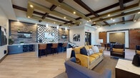 This single-floor amenity space is designed to serve as a dynamic social hub, offering a variety of distinct activity zones within one cohesive layout. The main lounge area immediately draws attention with its coffered ceiling adorned with dark wood beams, recessed lighting, and light wood-plank flooring that flows throughout. A marble-topped bar with leather barstool seating anchors one side of the room, backed by a striking geometric-patterned tile accent wall and pendant lighting. Adjacent seating areas feature contemporary furnishings, including a mustard yellow sofa and navy accent chairs, creating inviting conversation zones.

A game area incorporates a dedicated poker table and a billiards table, complemented by a bistro-style pub table with textured green accent walls and a mounted cue rack nearby. A media lounge with blue barrel chairs faces a wall-mounted flat-screen television, surrounded by large windows that admit natural light. Sliding reclaimed wood barn doors open into a private screening room, which features a tray ceiling with green accent lighting, patterned wallcovering, surround sound speakers, and plush lounge seating arranged toward a large display screen. Together, these zones create a well-appointed, versatile entertainment destination.