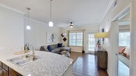 This thoughtfully designed single-floor residence offers a seamless blend of style and functionality across its open, well-connected layout. The kitchen serves as a centerpiece, featuring dark espresso cabinetry, granite countertops, a breakfast bar with pendant lighting, and black appliances — all visible from the entry. The bar-height counter with bar stools creates a natural gathering point that flows effortlessly into the living area.

The living room is warm and inviting, highlighted by rich hardwood flooring, crown molding, and a ceiling fan that adds to the comfortable ambiance. A large window and glass door flood the space with natural light, while the open sightlines from the kitchen make the area feel expansive and connected.

The bedroom is generously proportioned, offering ample room for a full furniture arrangement. It features hardwood flooring, a ceiling fan, and large windows that bring in soft natural light. The closet provides practical storage, completing the room's functional appeal.

The bathroom is accessed via a hallway and features a dark-cabineted vanity with a granite countertop, a well-lit mirror, and hardwood-style flooring that carries the cohesive aesthetic throughout. Crown molding and clean white walls tie all the spaces together, giving the residence a polished, unified character.