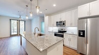 Located at 3250 Buford Hwy in Duluth, Georgia, this single-floor residence offers a thoughtfully designed layout with modern finishes and a clean, contemporary aesthetic. The kitchen serves as the centerpiece of the home, featuring a large granite-topped island with an undermount sink and stylish brass pendant lighting overhead. White shaker-style cabinetry lines the walls, complemented by a classic subway tile backsplash and a full suite of stainless steel appliances, including a side-by-side refrigerator, electric range, and built-in microwave. Warm hardwood-style flooring flows throughout the main living areas, creating a cohesive and inviting atmosphere. The living area benefits from natural light streaming through sliding glass doors that open to a private balcony, with a ceiling fan adding comfort to the space. The bedrooms are carpeted for warmth and offer generous proportions, with stylish gray-panel doors adding a modern touch. The bathrooms are well-appointed with granite vanity countertops, white cabinetry, and marble-style tile surrounds in the shower and tub areas. The primary bathroom includes a walk-in closet with built-in shelving. Throughout the residence, recessed lighting and a bright, neutral color palette create a fresh and welcoming environment.