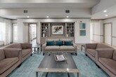 Located at 100 Stonegate Way in Middle Island, NY, this single-story community clubhouse offers a thoughtfully designed gathering space with a variety of amenities. The welcoming entrance features large glass doors and tile flooring that leads into the main areas of the building.

The centerpiece of the space is an elegant lounge area with warm hardwood-style flooring, recessed lighting, and a striking stone fireplace framed by a classic mantel. Large windows dressed with patterned drapery flood the room with natural light and offer views of the surrounding landscape. Comfortable, contemporary seating in neutral and teal tones creates an inviting atmosphere throughout.

Adjacent to the lounge, a dedicated billiards room features a full-size pool table beneath a stylish pendant chandelier, built-in shelving with cue storage, wainscoting details, and bar-height seating along the window wall.

Multiple dining areas provide flexible seating arrangements with dark wood tables and upholstered chairs, complemented by decorative built-ins and curated artwork. The fully equipped kitchen includes rich wood cabinetry, granite countertops, stainless steel appliances, and tile flooring, offering full functionality for community gatherings and events.