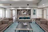 Located at 100 Stonegate Way in Middle Island, NY, this single-story community clubhouse offers a thoughtfully designed gathering space with a variety of amenities. The welcoming entrance features large glass doors and tile flooring that leads into the main areas of the building.

The centerpiece of the space is an elegant lounge area with warm hardwood-style flooring, recessed lighting, and a striking stone fireplace framed by a classic mantel. Large windows dressed with patterned drapery flood the room with natural light and offer views of the surrounding landscape. Comfortable, contemporary seating in neutral and teal tones creates an inviting atmosphere throughout.

Adjacent to the lounge, a dedicated billiards room features a full-size pool table beneath a stylish pendant chandelier, built-in shelving with cue storage, wainscoting details, and bar-height seating along the window wall.

Multiple dining areas provide flexible seating arrangements with dark wood tables and upholstered chairs, complemented by decorative built-ins and curated artwork. The fully equipped kitchen includes rich wood cabinetry, granite countertops, stainless steel appliances, and tile flooring, offering full functionality for community gatherings and events.