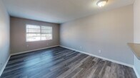 This single-floor unit offers a clean, modern aesthetic with thoughtfully updated finishes throughout. The living area is open and welcoming, featuring durable wood-style laminate flooring in a cool gray tone that lends a contemporary feel to the space. A standout architectural detail is the pass-through window connecting the living area to the kitchen, complete with a countertop overhang that functions as a convenient breakfast bar, enhancing the sense of openness between the two spaces.

The kitchen is efficiently designed with white shaker-style cabinetry, granite-look countertops, a stainless steel single-basin sink, and a stainless steel gas range with an overhead exhaust hood — offering a functional setup for everyday cooking.

The bedroom features plush carpeting for added comfort and includes a wide sliding-door closet that provides generous storage capacity. A second room, also with wood-style flooring, benefits from natural light streaming through a window fitted with blinds, making it a versatile space suitable as a bedroom or home office.

The bathroom is neatly appointed with wood-look flooring, a white vanity with mirror cabinet, and a full tub-shower combination with tiled surround. Throughout the unit, neutral wall tones and clean white trim create a bright, cohesive atmosphere that is move-in ready.