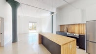 This 2-bedroom, 2-bathroom loft-style residence in Memphis, Tennessee offers an industrial-modern aesthetic rooted in thoughtful architectural detail. Polished concrete floors run throughout the entire unit, lending a clean, cohesive look that complements the bright white walls and soaring ceilings. A striking original cast-iron column with a decorative capital serves as a bold focal point in the open living and kitchen area, nodding to the building's historic character.

The open-concept kitchen is outfitted with dark lower cabinetry, a warm wood-toned backsplash, white upper cabinets, stainless steel appliances including a refrigerator and range, and a substantial butcher block island that doubles as additional prep and dining space. Pendant track lighting illuminates the area, and a sliding glass door opens to a balcony, flooding the living space with natural light.

Each bedroom features polished concrete floors, clean white walls, and access to generous walk-in closets. Tall windows and floor-to-ceiling sliding glass panels bring in abundant daylight. Both bathrooms are finished with gray double-drawer vanities, oval mirrors with modern black frames, globe pendant lighting, and glass-enclosed shower stalls — delivering a cohesive, contemporary feel throughout the home.
