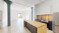 This 2-bedroom, 2-bathroom loft-style residence in Memphis, Tennessee offers an industrial-modern aesthetic rooted in thoughtful architectural detail. Polished concrete floors run throughout the entire unit, lending a clean, cohesive look that complements the bright white walls and soaring ceilings. A striking original cast-iron column with a decorative capital serves as a bold focal point in the open living and kitchen area, nodding to the building's historic character.

The open-concept kitchen is outfitted with dark lower cabinetry, a warm wood-toned backsplash, white upper cabinets, stainless steel appliances including a refrigerator and range, and a substantial butcher block island that doubles as additional prep and dining space. Pendant track lighting illuminates the area, and a sliding glass door opens to a balcony, flooding the living space with natural light.

Each bedroom features polished concrete floors, clean white walls, and access to generous walk-in closets. Tall windows and floor-to-ceiling sliding glass panels bring in abundant daylight. Both bathrooms are finished with gray double-drawer vanities, oval mirrors with modern black frames, globe pendant lighting, and glass-enclosed shower stalls — delivering a cohesive, contemporary feel throughout the home.