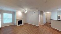 This single-story space in Lewisville offers a clean, functional layout anchored by an open living area. The room is finished with warm wood-style flooring that extends throughout, complementing the neutral gray walls and white baseboards that create a bright, cohesive aesthetic. A tile-surround fireplace serves as a focal point along one wall, adding a classic touch to the living space. The ceiling features a ceiling fan with a light fixture, providing both airflow and ambient lighting. Crown molding accents the upper portion of the walls, lending a refined detail to the interior. A hallway visible from the main living area leads to additional rooms, suggesting a practical and connected floor plan. Near the entrance, a white front door with hardware is framed by a clean entryway. HVAC vents are integrated into the ceiling, ensuring climate comfort throughout. The overall ambiance is neutral and move-in ready, with a straightforward design that balances functionality and comfort in a well-maintained single-level layout.