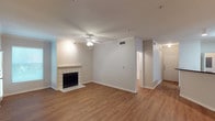 This single-story space in Lewisville offers a clean, functional layout anchored by an open living area. The room is finished with warm wood-style flooring that extends throughout, complementing the neutral gray walls and white baseboards that create a bright, cohesive aesthetic. A tile-surround fireplace serves as a focal point along one wall, adding a classic touch to the living space. The ceiling features a ceiling fan with a light fixture, providing both airflow and ambient lighting. Crown molding accents the upper portion of the walls, lending a refined detail to the interior. A hallway visible from the main living area leads to additional rooms, suggesting a practical and connected floor plan. Near the entrance, a white front door with hardware is framed by a clean entryway. HVAC vents are integrated into the ceiling, ensuring climate comfort throughout. The overall ambiance is neutral and move-in ready, with a straightforward design that balances functionality and comfort in a well-maintained single-level layout.