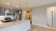 Located at 700 Corporate Center Dr in Raleigh, NC, this single-floor residence offers a thoughtfully designed layout with modern finishes throughout. The open-concept kitchen is a standout feature, showcasing sleek gray shaker-style cabinetry extending to the ceiling, stainless steel appliances including a French door refrigerator and range with microwave, a mosaic tile backsplash, and a generous island with granite countertops and a stainless undermount sink accented by polished pendant lighting. Light wood-style flooring flows seamlessly through the kitchen and into the open living area, which is outfitted with a ceiling fan and receives natural light through large windows offering views of the surrounding greenery. The bedrooms are bright and well-proportioned, each with ceiling fans, large windows, and the same warm flooring. The bathrooms are finished with gray cabinetry, granite countertops, marble-style tile surrounds, and wood-look flooring — one features a soaking tub and access to a walk-in closet, while another includes a walk-in tiled shower. A dedicated laundry area houses a full-size side-by-side washer and dryer. The overall ambiance is clean, contemporary, and move-in ready.