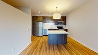 Located at 1300 W Lake St in Minneapolis, MN, this contemporary single-floor unit offers a clean, modern aesthetic throughout. The open-concept layout connects the kitchen and living areas seamlessly, creating a bright and functional living space. Light hardwood-style flooring runs throughout the main areas, lending warmth and continuity to the design.

The kitchen is a standout feature, equipped with dark espresso cabinetry that extends to the ceiling for ample storage, white subway tile backsplash, and a full suite of stainless steel appliances including a refrigerator, electric range, microwave, and dishwasher. A large central island with a crisp white countertop provides additional prep space and serves as a natural gathering point. Recessed lighting and a stylish drum pendant fixture illuminate the space effectively.

The living area is generously proportioned and benefits from a large picture window that invites natural light and offers views of the surrounding urban neighborhood. The open layout provides flexibility for a variety of furniture arrangements.

The bathroom features large-format gray tile flooring, clean white walls, and chrome fixtures, delivering a simple and polished finish. A barn-style sliding door adds a modern architectural touch to the unit's entryway corridor. Overall, the space presents a cohesive, contemporary design well-suited for urban living in the heart of Minneapolis.