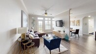 Located at 6500 Champion Grandview Way in Austin, Texas, this single-story residence offers a thoughtfully designed layout with a warm, modern aesthetic. An entry hallway with vaulted ceiling detail and a large paneled closet door leads into the main living area. The expansive living room features dark hardwood-style flooring, crown molding, a ceiling fan, and large windows and glass doors that invite abundant natural light. The open-plan layout connects seamlessly to a dining area, creating a generous and versatile living space. The kitchen is a standout feature, showcasing rich cherry wood cabinetry, stainless steel appliances, white countertops, track lighting, and a center island with bar seating — ideal for both cooking and casual dining. The bedrooms are carpeted for comfort, each featuring ceiling fans, ample natural light from wide windows, and generous proportions. The primary bedroom includes access to a full bathroom with a dual-sink vanity, white cabinetry, tile flooring, and a tub-shower combination. A second full bathroom mirrors this clean, functional design with its own dual-sink vanity and natural light. Throughout, the home maintains a cohesive neutral palette accented by warm wood tones, offering a refined yet inviting atmosphere.