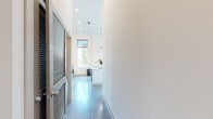 This contemporary Memphis residence offers a thoughtfully designed single-floor layout with two bedrooms and one bathroom. The open-concept living and kitchen area is an immediate standout, anchored by dramatic floor-to-ceiling glass doors that invite abundant natural light and frame outdoor views. The kitchen features white cabinetry, a central island, and pendant lighting, creating a clean and functional space. Polished concrete floors run throughout the living areas and bedrooms, lending an industrial-modern aesthetic that ties the entire unit together. The ceilings soar to impressive heights, amplifying the sense of openness throughout. The primary bedroom is generously sized and connects directly to a spacious walk-in closet outfitted with built-in shelving and hanging rods, as well as convenient access to the bathroom. A second bedroom benefits from large windows with lush outdoor views and tall ceilings, making it a bright and versatile space. The bathroom is elegantly appointed with a dual-sink vanity topped in white, white cabinetry with brushed hardware, a large mirror, and light-toned tile flooring, creating a serene, spa-like atmosphere. A hallway with recessed lighting and a louvered door completes the layout, offering a polished and cohesive feel throughout this modern Memphis home.