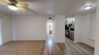 This single-floor, one-bedroom, one-bathroom residence offers a practical and comfortable layout across a compact, efficiently designed floor plan. The combined living and dining area serves as the heart of the home, featuring plush carpeting, a ceiling fan with light fixture, a textured ceiling, and a striking black tile-surround fireplace as a focal point. A sliding glass door with vertical blinds fills the living area with natural light and provides access to the outdoors. Hardwood-style flooring flows through the kitchen and hallways, contrasting nicely with the carpeted living and bedroom areas. The kitchen is well-appointed with gray cabinetry, granite-style countertops, black appliances including a refrigerator and range with overhead ventilation, and ample cabinet storage. A hallway connects the main living spaces to the private bedroom, which features its own ceiling fan, carpeted flooring, a window with natural light, and access to two closets offering generous storage. The bathroom includes a full tub and shower combo, toilet, and dark cabinetry with additional overhead storage. Textured ceilings and clean white walls throughout lend a consistent, neutral aesthetic to the entire space.