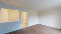 This two-floor residential space offers a practical and straightforward layout designed for comfortable everyday living. The main living area is generously sized, finished with neutral wall-to-wall carpeting and clean white walls that create a bright, open atmosphere. A large window fitted with vertical blinds allows natural light to fill the room, while a baseboard heating system runs along the perimeter. The living area connects seamlessly to the kitchen through an open pass-through window, offering a convenient visual connection between the two spaces. The galley-style kitchen features white cabinetry above and below the countertops, a stainless steel sink, light-toned laminate counters, and includes appliances such as a refrigerator, stove, and dishwasher. Vinyl flooring completes the kitchen's clean, functional look. Moving to the upper floor, the bedroom is distinguished by rich, warm hardwood flooring and a window that brings in natural light, with a baseboard heater providing warmth. The full bathroom is equipped with a tub and shower combination, a single vanity sink, a toilet, and parquet-style vinyl tile flooring. Throughout the space, the neutral color palette and clean finishes contribute to a simple, livable environment ready for personalization.