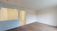 This two-floor residential space offers a practical and straightforward layout designed for comfortable everyday living. The main living area is generously sized, finished with neutral wall-to-wall carpeting and clean white walls that create a bright, open atmosphere. A large window fitted with vertical blinds allows natural light to fill the room, while a baseboard heating system runs along the perimeter. The living area connects seamlessly to the kitchen through an open pass-through window, offering a convenient visual connection between the two spaces. The galley-style kitchen features white cabinetry above and below the countertops, a stainless steel sink, light-toned laminate counters, and includes appliances such as a refrigerator, stove, and dishwasher. Vinyl flooring completes the kitchen's clean, functional look. Moving to the upper floor, the bedroom is distinguished by rich, warm hardwood flooring and a window that brings in natural light, with a baseboard heater providing warmth. The full bathroom is equipped with a tub and shower combination, a single vanity sink, a toilet, and parquet-style vinyl tile flooring. Throughout the space, the neutral color palette and clean finishes contribute to a simple, livable environment ready for personalization.