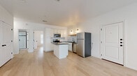 This single-story unit in Waco, Texas, offers a thoughtfully designed open-concept layout that maximizes its well-proportioned footprint. Light-toned hardwood flooring flows consistently throughout the space, creating a cohesive and clean aesthetic from room to room.

The combined kitchen and living area forms the heart of the unit. The kitchen is outfitted with white shaker-style cabinetry, dark granite countertops, a white subway tile backsplash, and a full suite of stainless steel appliances including a refrigerator, range, microwave, and dishwasher. A central island with a dark granite top provides additional workspace and storage. A natural wood open shelf and brass-toned wall sconces add warm, modern character. The living area benefits from large windows that invite natural light and offer views of the surrounding area, complemented by a ceiling fan with recessed lighting overhead.

The bedroom is a calm, bright space with continued hardwood flooring, access to a spacious walk-in closet featuring built-in shelving and hanging rods. The bathroom features a glass-enclosed walk-in shower with white tile surround and dark accent trim, paired with matte black hardware for a contemporary finish.