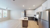 Located in O'Fallon, Missouri, this well-appointed 3-bedroom, 3-bathroom single-story home offers a thoughtfully designed open-concept layout. The kitchen and living area form the heart of the home, showcasing a striking two-tone cabinet design with dark espresso lower cabinets and crisp white upper cabinetry, complemented by light quartz countertops and a full suite of stainless steel appliances. A central island with a built-in sink adds both functionality and style, while light wood-tone flooring flows seamlessly throughout the entire home, creating a bright and cohesive aesthetic.

The living area benefits from natural light through large windows and features a ceiling fan, lending a comfortable, airy feel. Each of the three bedrooms is well-proportioned, with the spacious primary bedroom offering ample room and dedicated closet space. The bathrooms are well-finished, with one featuring a sleek glass-enclosed walk-in shower and dark wood vanity with white countertop, while another offers a tub/shower combo. A dedicated in-unit laundry room houses a full-size washer and dryer with additional wire shelving above. Three closets and a hallway round out this practical and modern home.