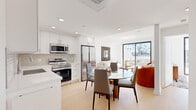 Located on Beverly Boulevard in Los Angeles, this modern 1-bedroom, 1-bathroom unit offers a thoughtfully designed open-concept layout bathed in natural light. Light hardwood flooring flows throughout, unifying the kitchen, dining, and living areas into a cohesive, airy space.

The kitchen is outfitted with sleek white cabinetry extending to the ceiling, a subway tile backsplash, stainless steel appliances including a full-size refrigerator and range with overhead microwave, and a dishwasher. A circular glass dining table sits adjacent, creating a seamless transition into the living room.

The living room is highlighted by a skylight and large sliding glass doors that open directly onto a private rooftop terrace. The terrace offers sweeping views of the Los Angeles skyline and iconic palm trees, with ample space for outdoor seating. The bedroom continues the bright, minimalist aesthetic, featuring its own sliding glass door to the terrace, a mirrored sliding closet, and generous natural light.

The bathroom is clean and contemporary, with a tub-shower combination enclosed by sliding glass panels, a large backlit vanity mirror, white cabinetry, and matching light wood flooring. Throughout the unit, recessed lighting and crisp white walls reinforce the modern, understated character of this well-appointed Los Angeles residence.