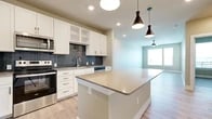 This thoughtfully designed 1-bedroom, 1-bathroom residence offers a functional and modern single-floor layout. The open-concept kitchen and living area serves as the heart of the home, featuring crisp white shaker cabinetry, a striking slate-blue tile backsplash, quartz countertops, and a full suite of stainless steel appliances including a refrigerator, range, microwave, and dishwasher. A large central island with pendant lighting above provides additional prep space and casual seating. Light wood-tone flooring flows consistently throughout the unit, complementing the neutral, warm wall tones.

The living area extends naturally from the kitchen, benefiting from a ceiling fan and a window that brings in natural light. The bedroom is a comfortable, well-proportioned retreat with its own ceiling fan, large windows offering outdoor views, and light hardwood-style flooring. It connects directly to the full bathroom, which includes a white vanity with quartz countertops, brushed hardware, and a tiled walk-in shower. A generously sized walk-in closet with built-in shelving and hanging rods is accessible directly from the bathroom, offering ample organized storage. The overall aesthetic is clean, contemporary, and move-in ready.