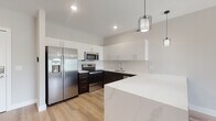 Located at 5711 Menerey Ln in Columbus, Ohio, this modern single-floor residence showcases a clean, contemporary design with consistent luxury vinyl plank flooring and a neutral color palette throughout. The kitchen is a standout feature, equipped with stainless steel appliances including a French door refrigerator, electric range, microwave, and dishwasher. Dark espresso lower cabinetry is elegantly contrasted by crisp white upper cabinets, all accented by a white quartz countertop and a geometric hexagonal tile backsplash. A large kitchen island provides additional prep and dining space, while stylish industrial-style pendant lights add a modern finishing touch. The bedroom offers a bright and airy atmosphere, benefiting from a large window with horizontal blinds that invite natural light and provide views of the surrounding neighborhood. The bathroom is well-appointed with a backlit vanity mirror, a white quartz single-sink vanity, light cabinetry, and a full-size soaking tub with a tiled surround. The layout, as revealed in the dollhouse view, includes a thoughtfully arranged floor plan with clearly defined living, sleeping, and bathroom areas, all connected by an open and efficient flow. The consistent light-toned flooring and soft gray walls contribute to a cohesive and welcoming ambiance throughout the entire space.