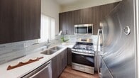 This two-story residence on Harlow Avenue in Los Angeles is designed with a clean, modern aesthetic throughout. The main level features an open living area anchored by a fireplace and framed by multiple windows with vertical blinds that invite generous natural light. Rich, dark hardwood-style flooring extends through the living and dining areas, creating a warm contrast against the crisp white walls. A breakfast bar connects the dining space to the kitchen, which is outfitted with dark espresso cabinetry, light quartz countertops, a tile backsplash, and a full suite of stainless steel appliances including a gas range, built-in microwave, dishwasher, and refrigerator.

A staircase leads to the upper level, where the bedrooms are finished with plush carpeting. One bedroom features a walk-in closet, while another includes mirrored sliding closet doors that add depth to the room. The bathrooms are well-appointed, with one featuring a vessel sink atop a dark vanity with wood-look flooring, and another offering a tub-shower combination. The overall ambiance of the space is bright, clean, and functional, offering a comfortable layout suited for everyday living.
