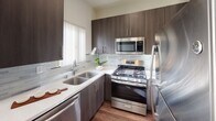 This two-story residence on Harlow Avenue in Los Angeles is designed with a clean, modern aesthetic throughout. The main level features an open living area anchored by a fireplace and framed by multiple windows with vertical blinds that invite generous natural light. Rich, dark hardwood-style flooring extends through the living and dining areas, creating a warm contrast against the crisp white walls. A breakfast bar connects the dining space to the kitchen, which is outfitted with dark espresso cabinetry, light quartz countertops, a tile backsplash, and a full suite of stainless steel appliances including a gas range, built-in microwave, dishwasher, and refrigerator.

A staircase leads to the upper level, where the bedrooms are finished with plush carpeting. One bedroom features a walk-in closet, while another includes mirrored sliding closet doors that add depth to the room. The bathrooms are well-appointed, with one featuring a vessel sink atop a dark vanity with wood-look flooring, and another offering a tub-shower combination. The overall ambiance of the space is bright, clean, and functional, offering a comfortable layout suited for everyday living.