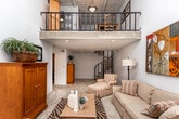 Located at 1049 Powers Ferry Rd SE in Marietta, Georgia, this two-story home offers a well-organized layout with comfortable living spaces across both levels. The living room makes an immediate impression with its soaring vaulted ceilings, oversized sliding glass doors, and transom windows that bathe the space in natural light while framing serene views of the surrounding wooded landscape. Vertical blinds provide privacy while preserving the airy, open feel of the room.

The dining area is situated on the upper level and is distinguished by a decorative textured ceiling, a pendant light fixture, and a wrought iron railing overlooking the staircase below. Large windows in this area continue the theme of greenery-filled views.

The kitchen is equipped with white cabinetry, ample counter space, a double stainless steel sink, and a window that lets in natural light. The hardwood-style flooring carries through into the bathrooms, both of which feature white vanities with generous countertops, mirrors, and shower-tub combinations.

The bedrooms offer carpeted flooring and a restful atmosphere. The primary bedroom includes a closet, while a second bedroom is well-appointed with natural light and wall décor. The staircase connecting the two floors serves as a central architectural feature, anchoring the home's open, multi-level design.
