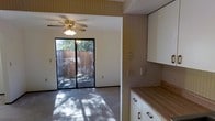 This multi-story space is spread across three floors, offering a versatile layout suited for a variety of uses. The main living area is bright and welcoming, featuring a ceiling fan with light fixture and large sliding glass doors that open to an outdoor patio area. Natural light filters through the doors, casting dappled patterns across the carpeted floor and creating a warm, inviting ambiance. The striped wallcovering adds a classic, textured character to the walls throughout the space.

Adjacent to the living area, the kitchen is efficiently designed with clean white cabinetry, a butcher block-style countertop, and ample storage. The open connection between the kitchen and living area promotes a functional flow, making the space practical for everyday living.

The sliding glass doors provide a direct view of a private, fenced outdoor area, enhancing the sense of connection to the exterior. With three floors of living space, this property offers generous room to accommodate diverse needs, from private retreats to shared living areas. The overall aesthetic blends classic design elements with practical functionality throughout each level.