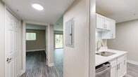 This 1-bedroom, 1-bathroom unit in Greenville, SC offers a clean, modern layout across a single floor. The living room is a standout space, featuring durable gray wood-look flooring, neutral warm-toned walls, a ceiling fan, and a large sliding glass door that floods the room with natural light and frames lush green outdoor views. The galley-style kitchen is efficiently designed with white shaker cabinetry, white quartz countertops, a stainless steel sink, and a full suite of stainless steel appliances including a refrigerator, range, and over-the-range microwave. The kitchen connects seamlessly to the hallway, which leads to the remaining rooms. The spacious primary bedroom offers ample room, a window with natural light, neutral gray walls, and matching wood-look flooring. A dedicated closet with built-in rods provides convenient storage. The bathroom features a white vanity with quartz countertop, a framed mirror, wood-look tile flooring, and a tub-shower combination with tiled surround. Throughout the unit, consistent flooring, clean white trim, and a neutral color palette create a cohesive and contemporary aesthetic.
