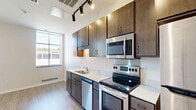 Located at 1667 Snelling Ave N in Falcon Heights, Minnesota, this efficiently designed unit offers a thoughtful layout that maximizes every square foot of its compact footprint. The open-concept living and kitchen area is anchored by a sleek, modern kitchen featuring rich dark wood cabinetry, light granite-style countertops, and a full suite of stainless steel appliances including an electric range, over-the-range microwave, dishwasher, and refrigerator. Track lighting illuminates the kitchen workspace, while recessed lighting adds a clean, contemporary touch throughout. Light wood-look luxury vinyl flooring runs continuously through the space, lending warmth and visual continuity. The living area is bright and open, with a large window that invites natural light and a view of the surrounding greenery. A bold navy entry door adds a modern design accent at the front of the unit. The bathroom is clean and functional, outfitted with a full tub/shower combination, brushed nickel fixtures, a vanity with storage, and matching light flooring. The overall aesthetic is modern and neutral, offering a move-in-ready canvas well suited for comfortable urban living.