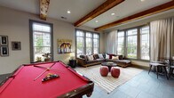 The Springhouse Apartments clubhouse is a thoughtfully designed single-story community facility that blends rustic architectural elements with modern amenities. The entrance foyer sets a welcoming tone with soaring ceilings, hardwood flooring, and oversized windows that frame views of the surrounding community. Elegant wingback chairs and a plush sofa create an inviting seating area near the grand double entry doors, which are topped with transom windows that draw in abundant natural light.

Moving further inside, the main lounge area is distinguished by exposed wooden ceiling beams that lend a warm, rustic character to the space. Floor-to-ceiling windows on multiple walls flood the room with natural light and offer panoramic outdoor views. A large sectional sofa anchors a comfortable conversation area, while a full-sized billiards table with a bold red felt surface serves as a central recreational feature. Sliding barn doors in a rich red finish add a charming design detail that ties the space together.

The fitness center is generously proportioned and well-equipped, featuring a wide array of strength-training machines, free weights, weight benches, treadmills, ellipticals, and TRX suspension equipment. Bold red accent walls, large mirrors, mounted televisions, and abundant natural light from surrounding windows create an energizing environment for residents.