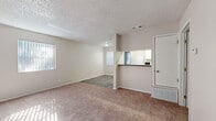 This single-story residence offers a practical and efficiently designed floor plan, accommodating two bedrooms and two bathrooms within a well-utilized living space. The open living room is carpeted in a warm neutral tone and benefits from multiple windows fitted with vertical blinds, allowing natural light to filter throughout. A textured popcorn ceiling and light beige walls contribute to the space's clean, understated aesthetic. The living area transitions seamlessly toward the kitchen via a half-wall pass-through with a dark countertop, providing visual connectivity while maintaining a defined separation. The galley-style kitchen features white cabinetry, tile backsplash, wood-look vinyl flooring, and white appliances including a refrigerator and electric range. Both bedrooms are carpeted and offer a quiet, neutral atmosphere, with windows providing natural light. The primary bedroom is a comfortable size and includes access to a closet. A walk-in closet with double hanging rods and wood-look flooring provides ample storage. The bathrooms include a full tub-shower combination with white tile surround and chrome fixtures. Throughout the residence, consistent neutral tones and clean finishes create a cohesive, move-in ready environment.