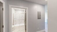 Located at 365 Western Ave in Boston's Brighton neighborhood, this thoughtfully designed one-bedroom, one-bathroom residence offers a clean, modern aesthetic throughout. Light gray walls, crisp white trim, and wide-plank wood-style flooring create a cohesive, contemporary look across the entire floor plan.

The kitchen is well-appointed with shaker-style cabinetry, white quartz countertops, a subway tile backsplash, and a full suite of stainless steel appliances including a gas range, built-in microwave, dishwasher, and refrigerator. The open living area is bright and airy, with recessed lighting and a glass-panel door leading to a private balcony with city views.

The bedroom features a large picture window framing urban Boston views, along with direct access to a dedicated closet with built-in rod storage. A separate closet area in the hallway houses a stacked washer and dryer, adding convenient in-unit laundry.

The bathroom is finished to a high standard, showcasing marble-look porcelain wall tile in the walk-in shower with a frameless sliding glass door in brushed gold, complemented by hexagonal tile flooring and a clean white vanity. A smart thermostat and modern panel complete the space's practical amenities.
