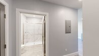 Located at 365 Western Ave in Boston's Brighton neighborhood, this thoughtfully designed one-bedroom, one-bathroom residence offers a clean, modern aesthetic throughout. Light gray walls, crisp white trim, and wide-plank wood-style flooring create a cohesive, contemporary look across the entire floor plan.

The kitchen is well-appointed with shaker-style cabinetry, white quartz countertops, a subway tile backsplash, and a full suite of stainless steel appliances including a gas range, built-in microwave, dishwasher, and refrigerator. The open living area is bright and airy, with recessed lighting and a glass-panel door leading to a private balcony with city views.

The bedroom features a large picture window framing urban Boston views, along with direct access to a dedicated closet with built-in rod storage. A separate closet area in the hallway houses a stacked washer and dryer, adding convenient in-unit laundry.

The bathroom is finished to a high standard, showcasing marble-look porcelain wall tile in the walk-in shower with a frameless sliding glass door in brushed gold, complemented by hexagonal tile flooring and a clean white vanity. A smart thermostat and modern panel complete the space's practical amenities.