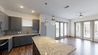 This well-appointed single-floor residence combines modern design with functional living. The heart of the home is a gourmet kitchen showcasing a large granite island, gray shaker-style cabinetry, a subway tile backsplash, and a full suite of stainless steel appliances including a refrigerator, range, and built-in microwave. Elegant glass pendant lights hang above the island, adding a refined touch. Rich, dark hardwood-style flooring runs throughout the main living areas, complementing the neutral palette of the walls.

The open living area is bathed in natural light, courtesy of floor-to-ceiling glass doors that lead to a private balcony, offering views of the surrounding neighborhood. A ceiling fan provides additional comfort in this generous space.

The bedrooms are carpeted for warmth and comfort, each featuring large windows that invite natural light and outdoor views. The bathroom is thoughtfully finished with granite countertops, gray cabinetry, an undermount sink, a wide vanity mirror, and a tub-shower combination adorned with elegant marble-style tile surround and a built-in niche. Clean lines and consistent finishes throughout create a cohesive, modern aesthetic across the entire residence.
